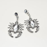 Scorpion-shaped earrings with crystal details on a light gray background